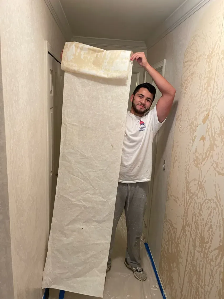 Man holding a long, rolled-up insulation panel in a hallway with wallpaper.