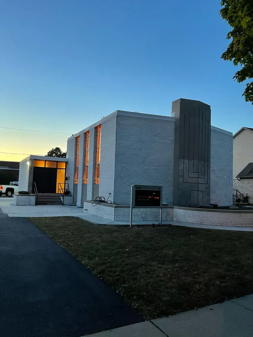 Modern, light-colored building with vertical windows and a dark entryway under a blue dusk sky.