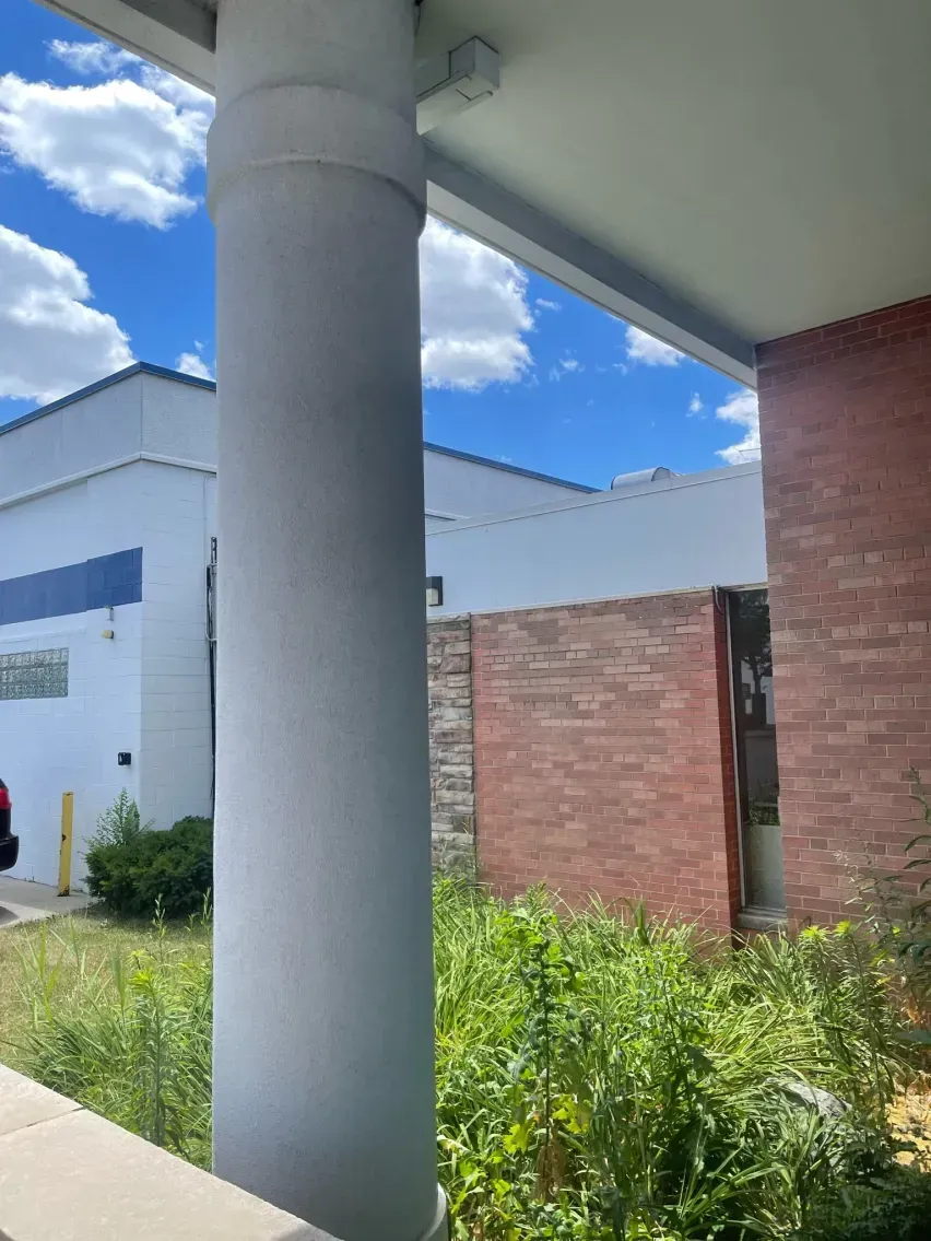 White column in front of a building with red brick and white walls, blue sky in background.