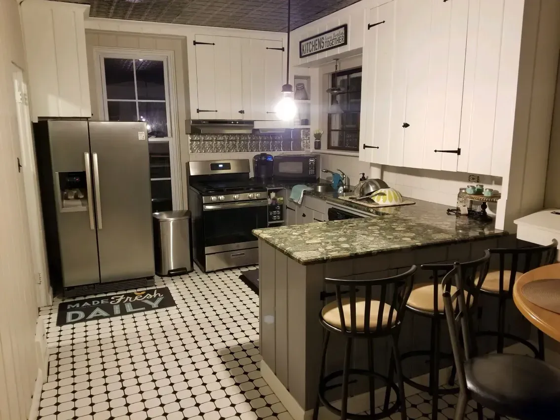 Kitchen with white cabinets, stainless steel appliances, and a small island with stools.