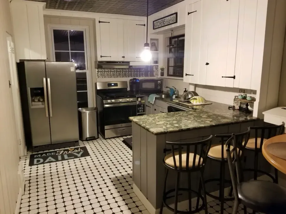 Kitchen with white cabinets, stainless steel appliances, black and white tile floor, and a small island with seating.