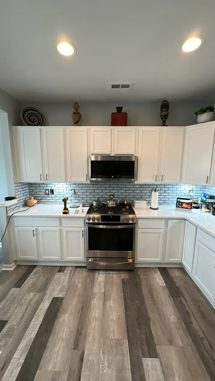White kitchen with stainless steel appliances, white cabinets, grey countertops, and wood-look flooring.