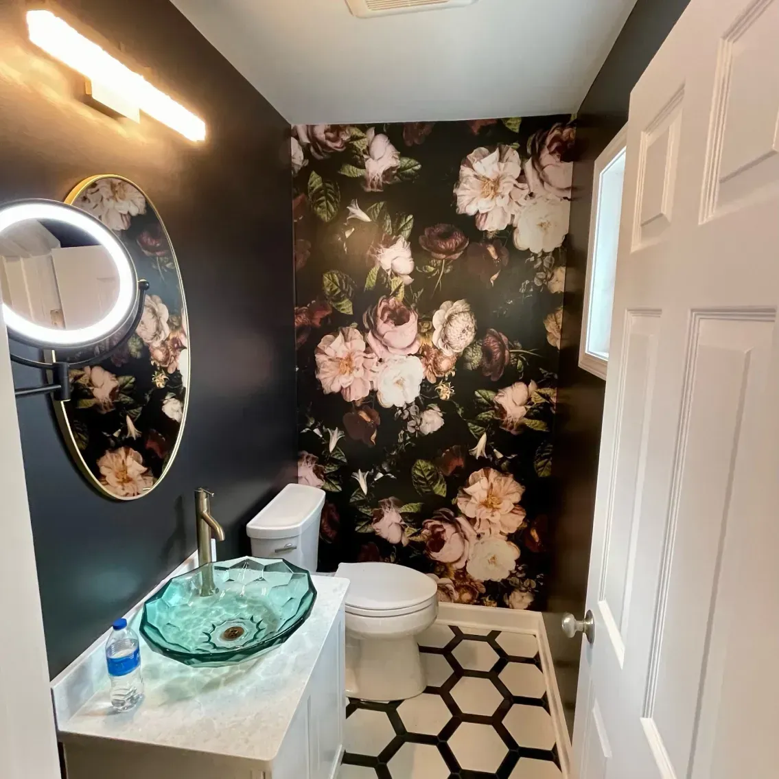 Small bathroom with floral wallpaper, black and white hexagon floor tiles, and a glass sink.