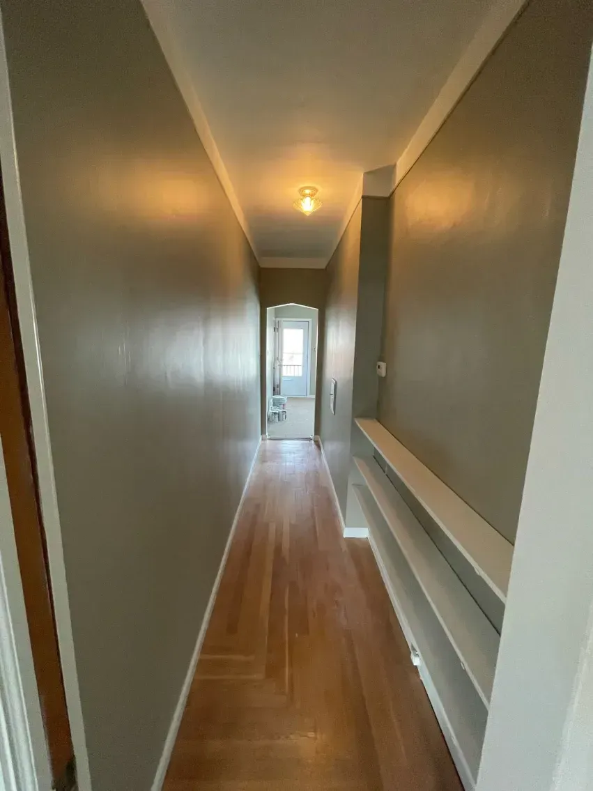 Narrow hallway with gray walls, wooden floor, and built-in white shelves.