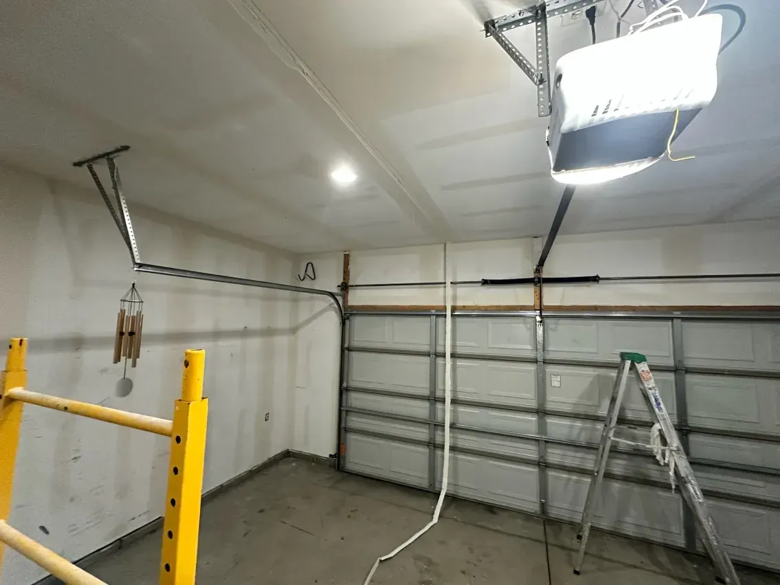 Garage interior with an open door, ladder, and garage door opener.