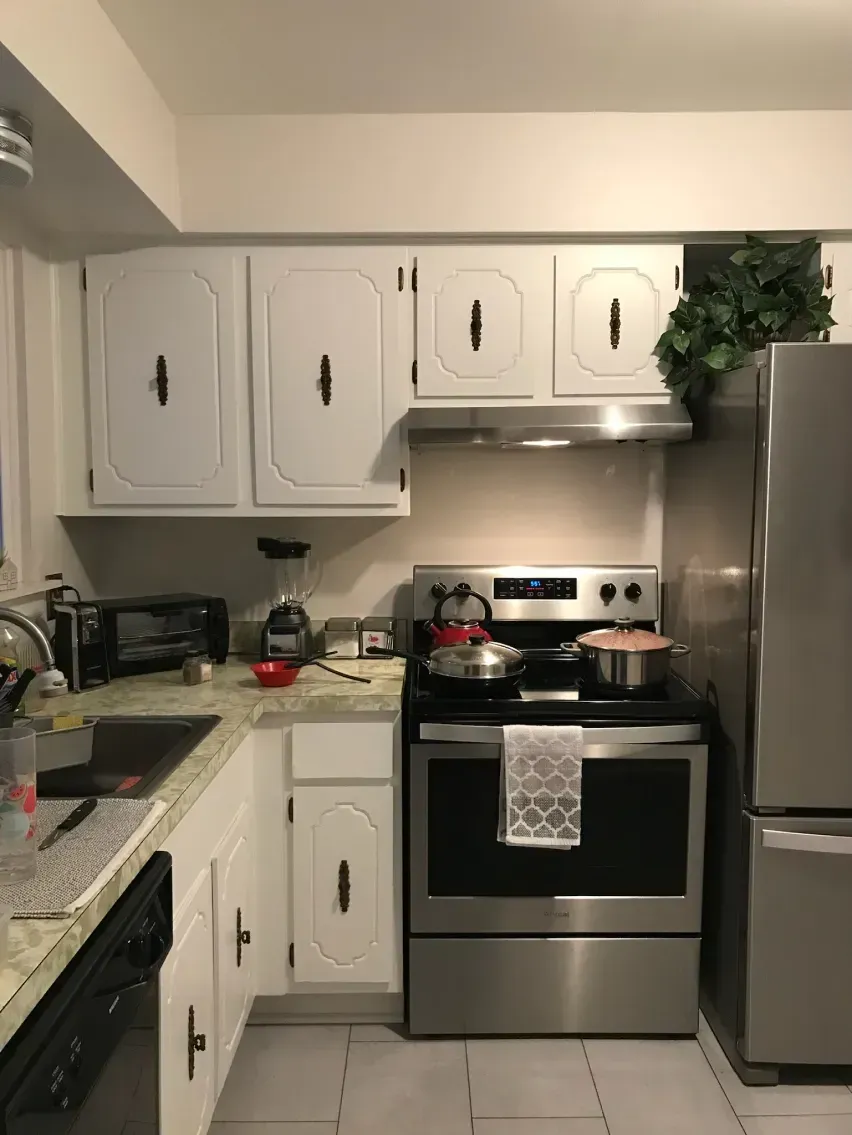 White kitchen with stainless steel appliances, white cabinets, and a gray countertop.