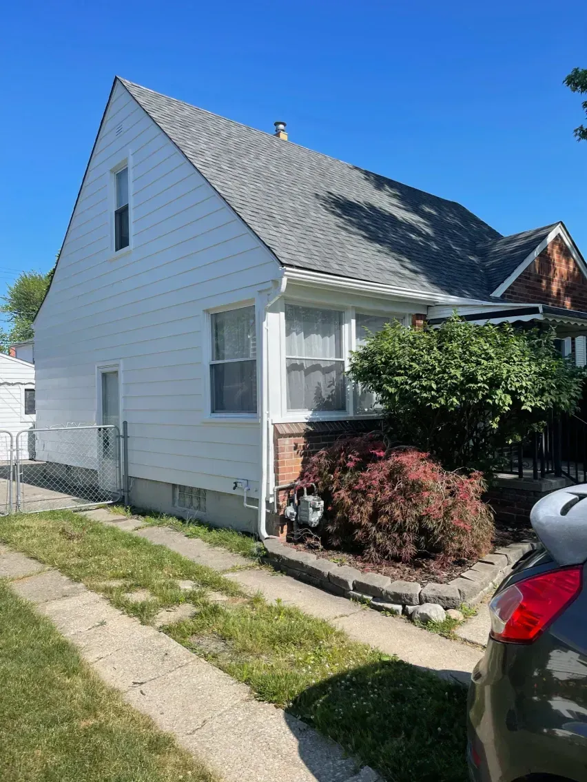 White house with gray roof, small yard, and driveway under a clear, blue sky.