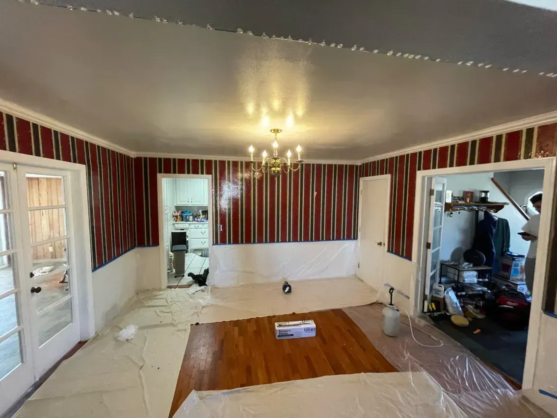 Room being renovated, with shiny ceiling and red striped walls, doorway on each side, light wood floor.