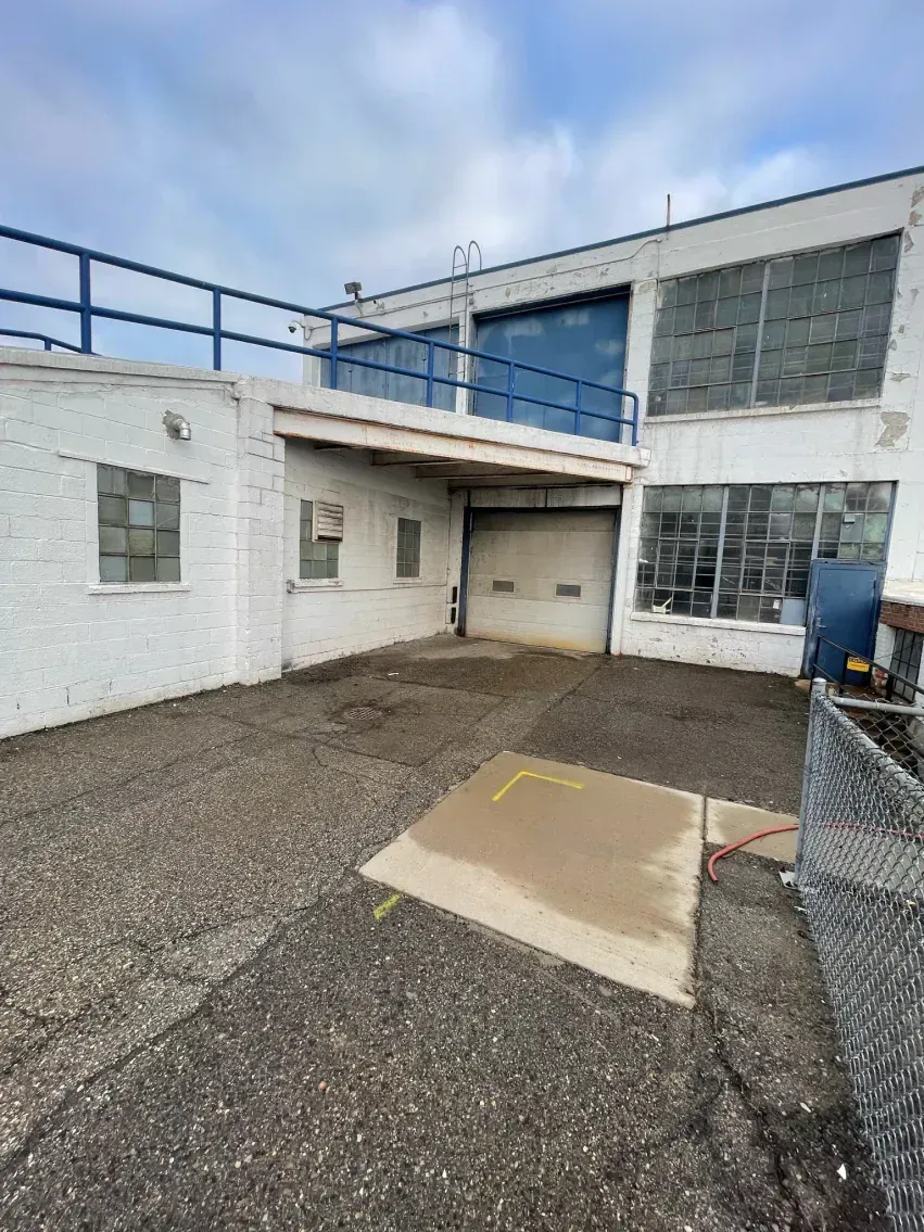 Exterior of a white industrial building with a loading dock, gravel, concrete, and a blue railing.