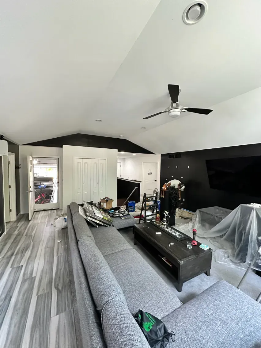 Living room with gray sofa, dark walls, white ceiling, and a ceiling fan.