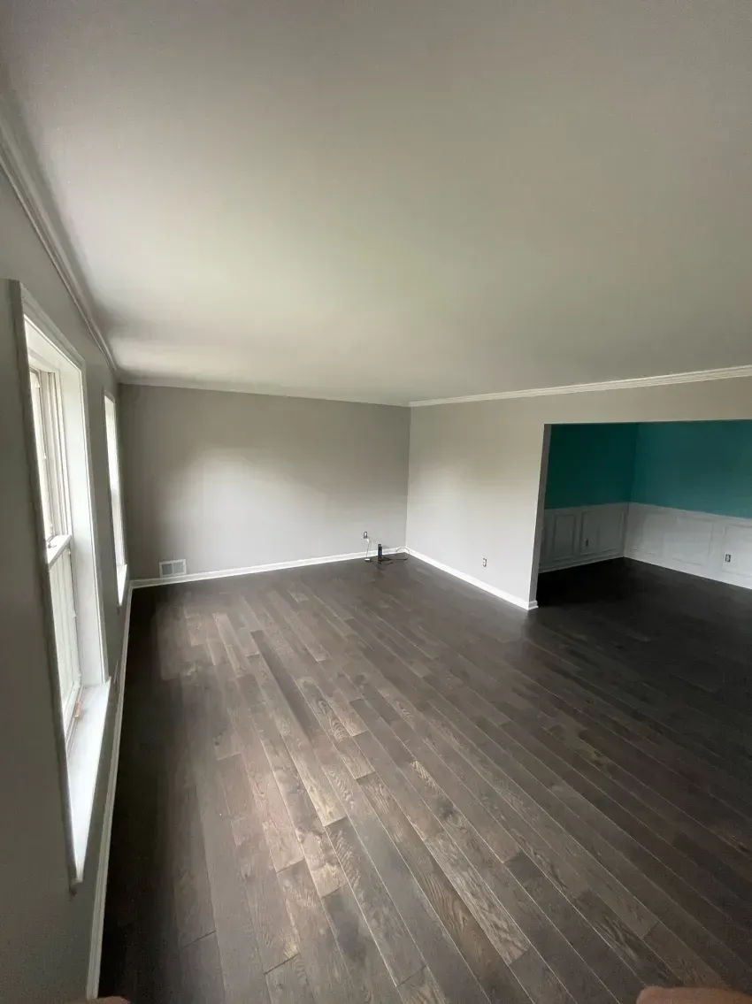 Empty living room with dark wood floor, gray walls, white trim, and a turquoise accent wall.