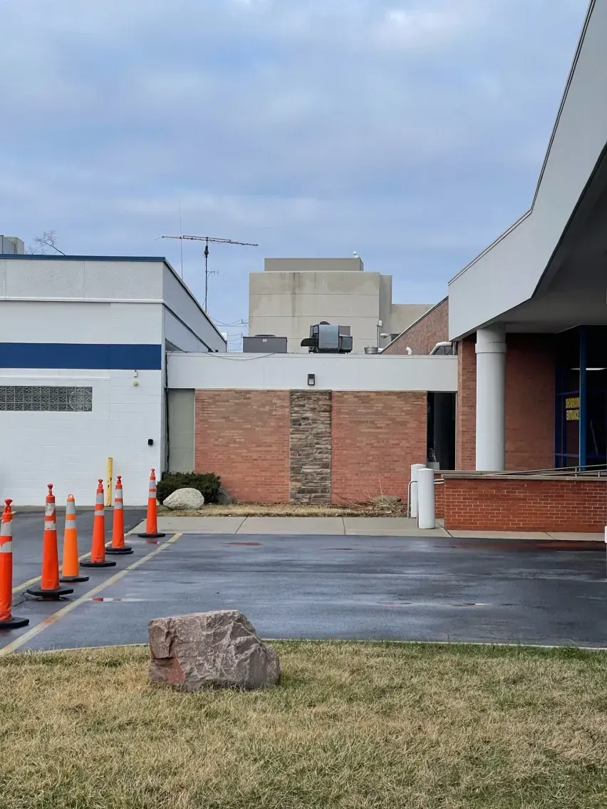 Building exterior with brick and white sections, orange traffic cones, and cloudy sky.