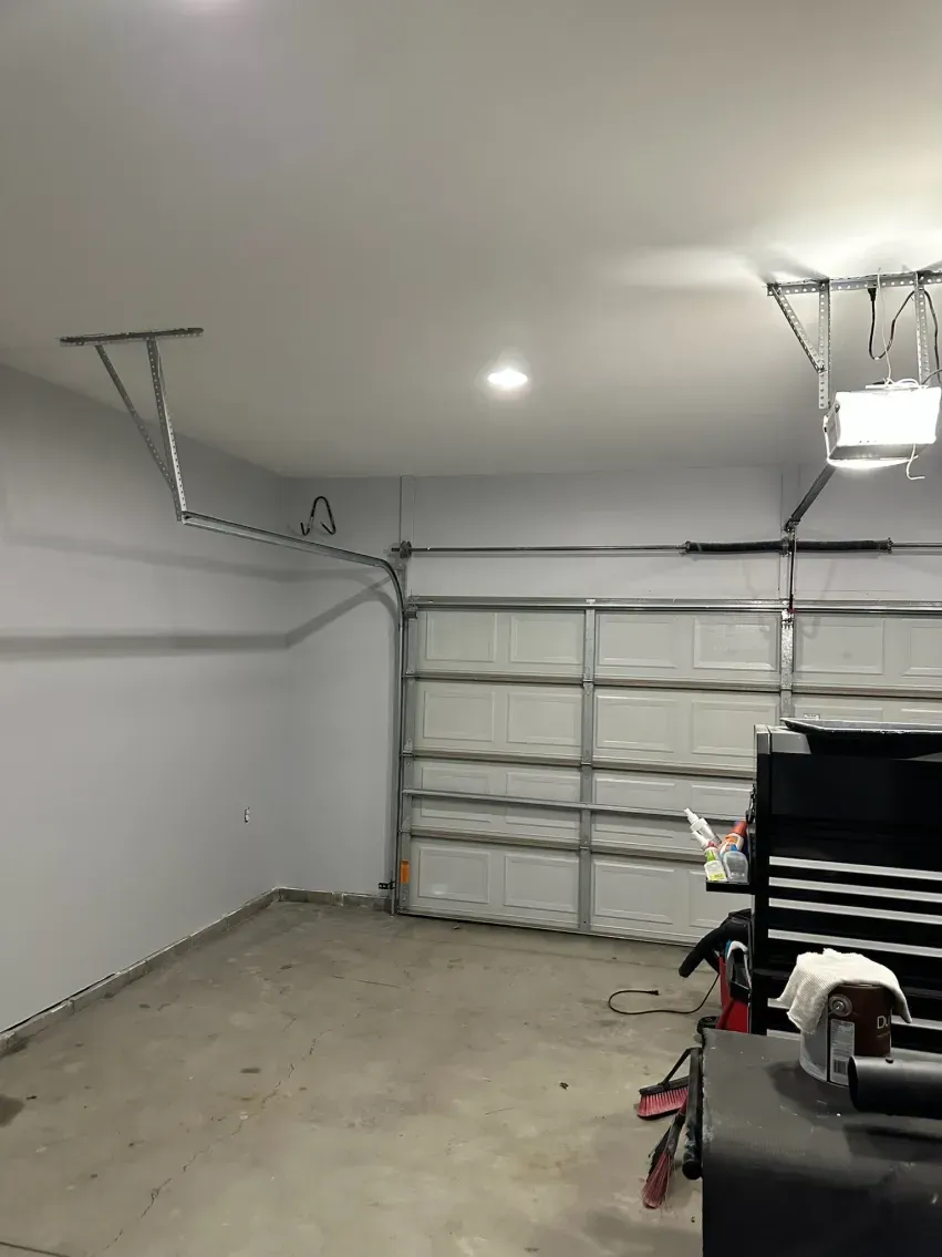 Interior of a garage with a closed garage door, white walls, and a tool chest.