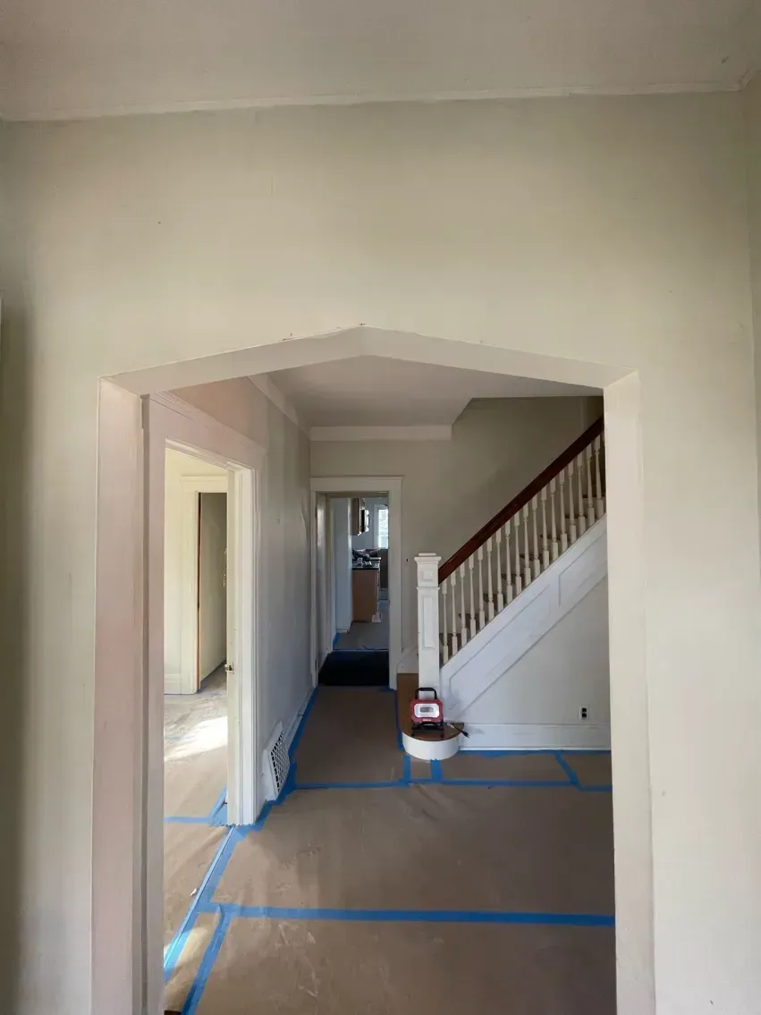 Interior view: doorway archway leading to hallway with stairs. Construction tape on floor.