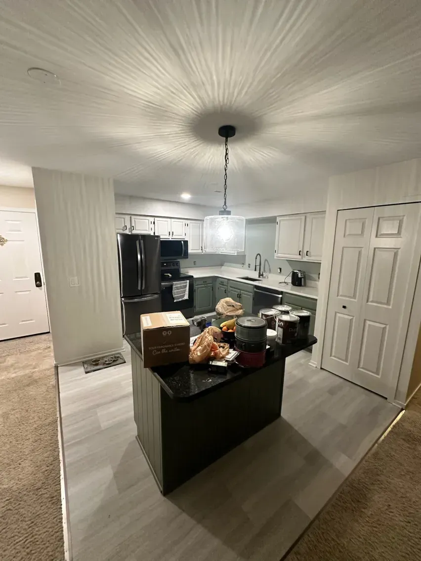 Kitchen with dark island, black appliances, white cabinets, and gray flooring.