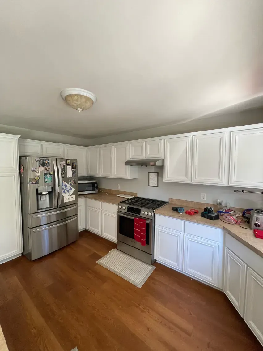 White kitchen with stainless steel appliances, wood cabinets, and wood flooring.