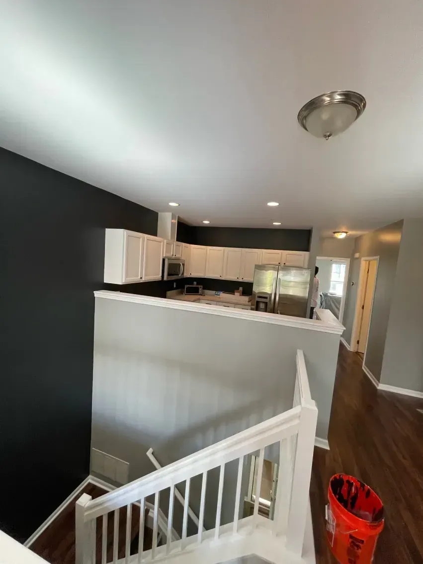 View from stairs looking into a kitchen with white cabinets, dark gray walls, and hardwood floors.