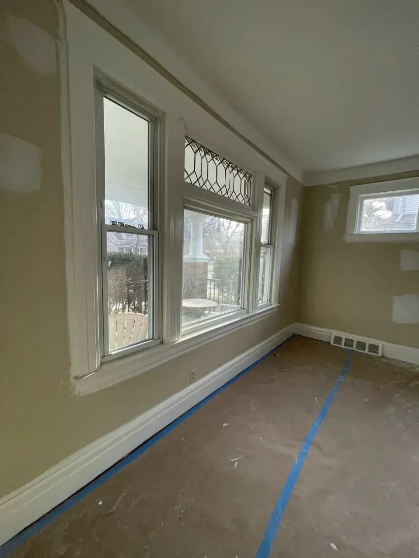Interior view of a room with windows and light-colored walls. Blue tape on the floor.