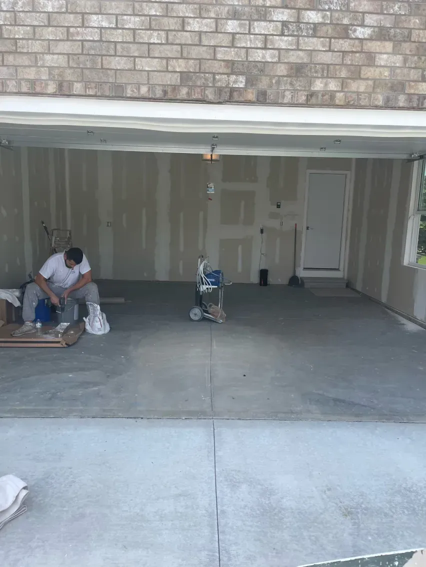 Man working in a garage under construction; concrete floor, drywall, brick exterior.