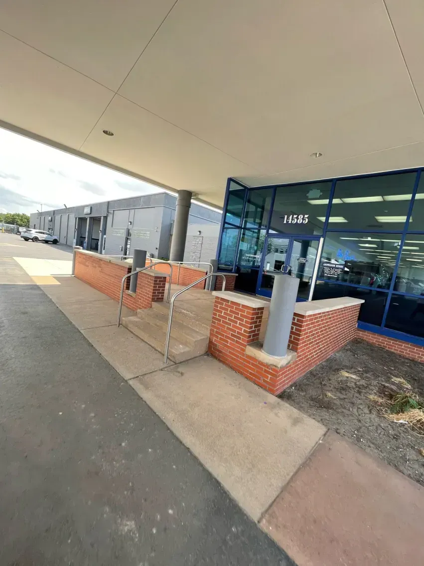 Building entrance with ramp. Red brick walls, glass door, concrete path under awning.