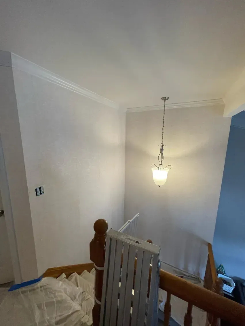 View of a stairwell with a hanging light fixture and painted walls. Wooden railing and steps are visible.