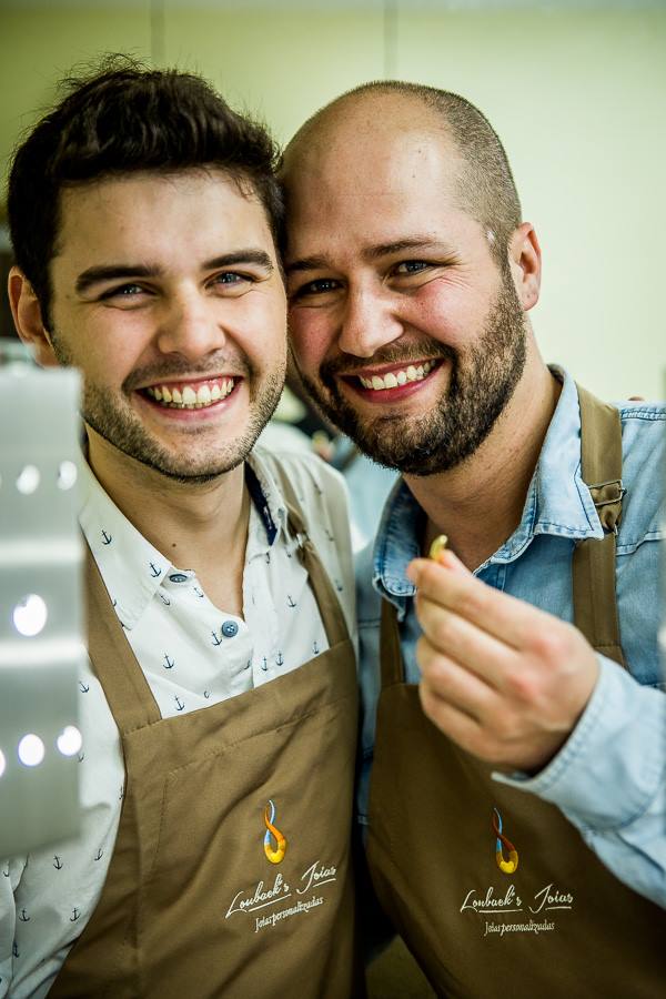 Dois homens vestindo aventais estão próximos um do outro e sorrindo.