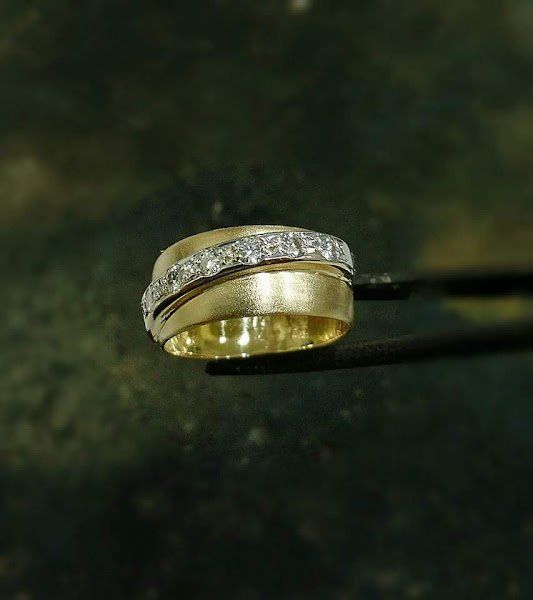 Um anel de ouro com diamantes está sendo segurado por uma pinça