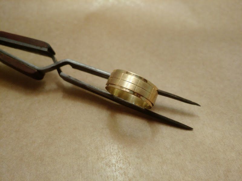 Uma pinça segurando um anel de ouro sobre uma mesa