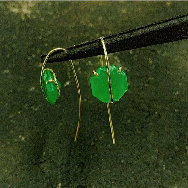 Um par de brincos verdes está sendo segurado por um par de pauzinhos