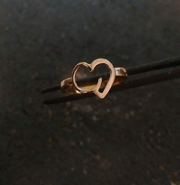 Um anel dourado em forma de coração está sendo segurado por uma pinça