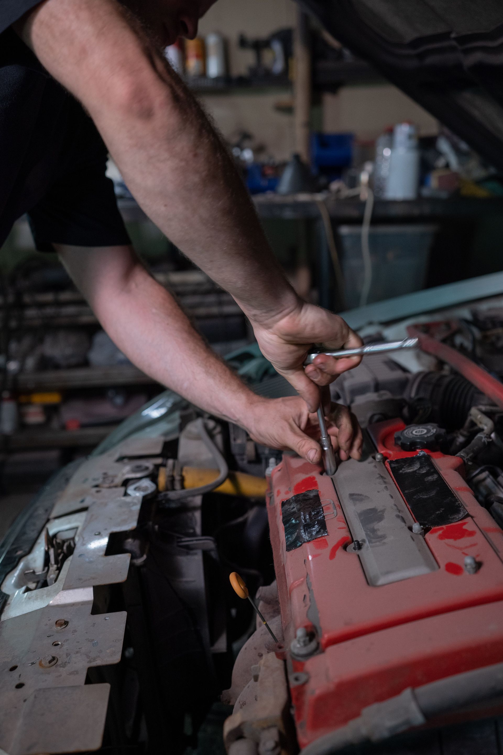 Mechanic working on a car engine, inspecting with a tool.