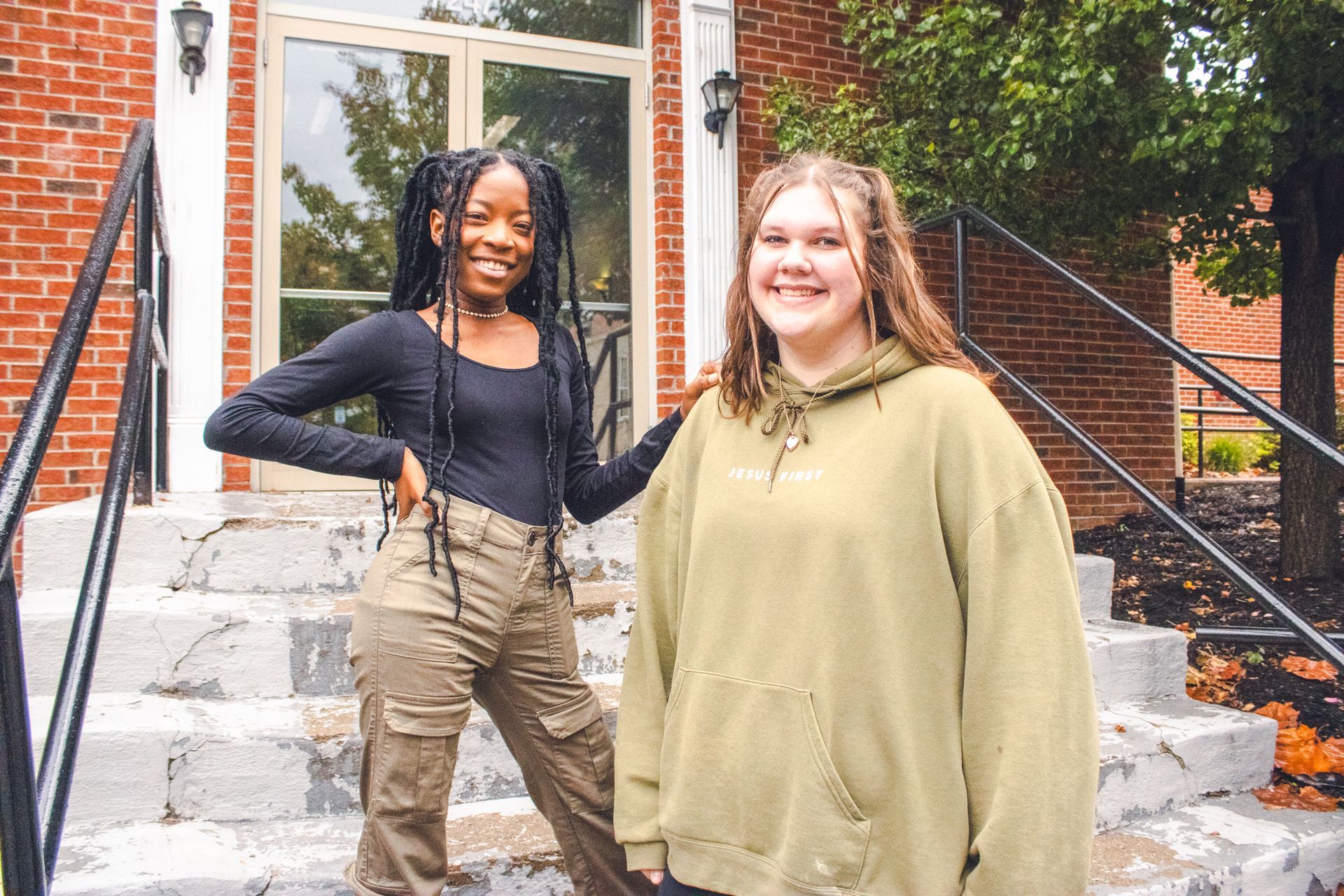 Two young women are standing next to each other on the steps of the cafeteria