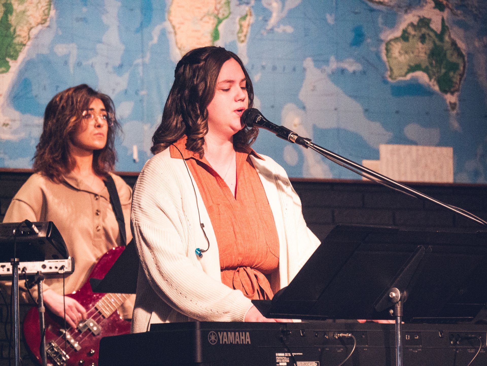 A woman singing into a microphone next to a yamaha keyboard