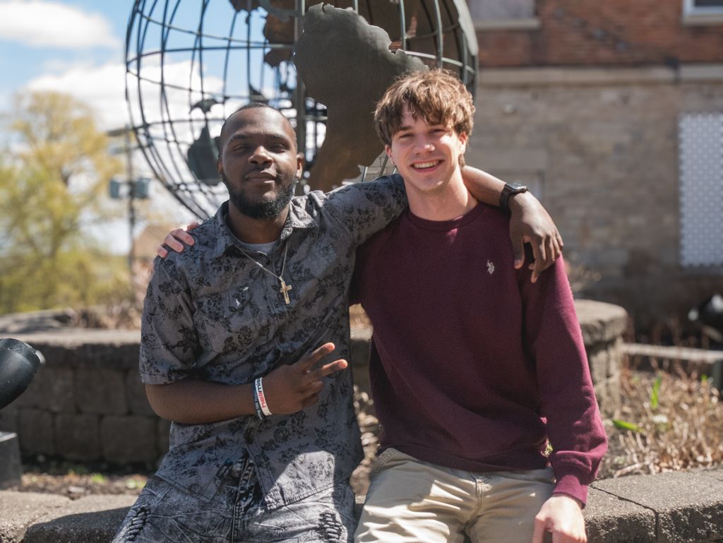 Two young men are posing for a picture in front of a statue of a globe.