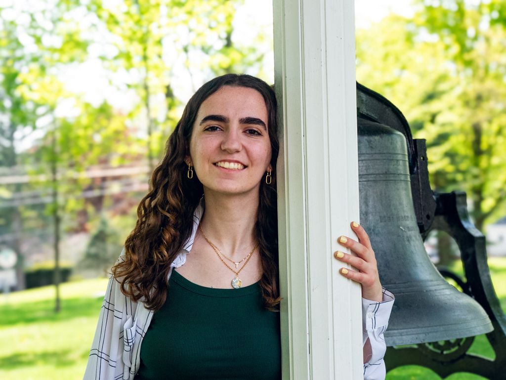 A female student smiles in front of the old Elim bell.
