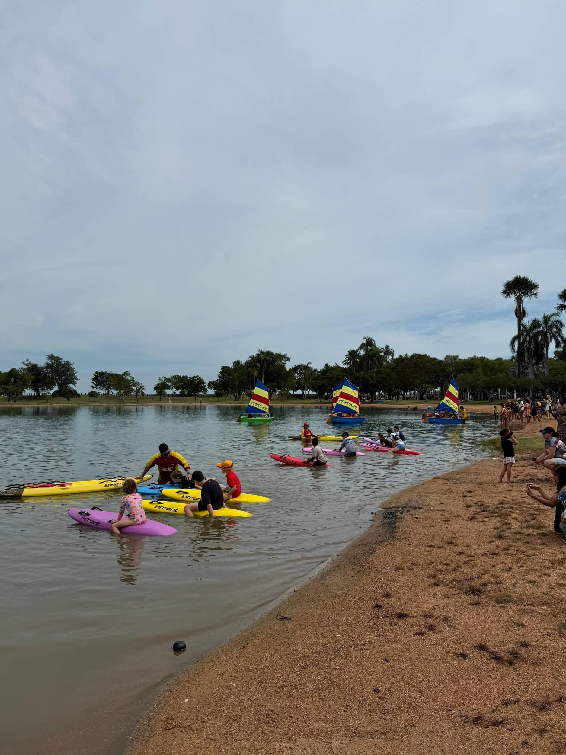 People kayaking on a calm river near a rocky shore, with colorful kayaks and umbrellas in the distance