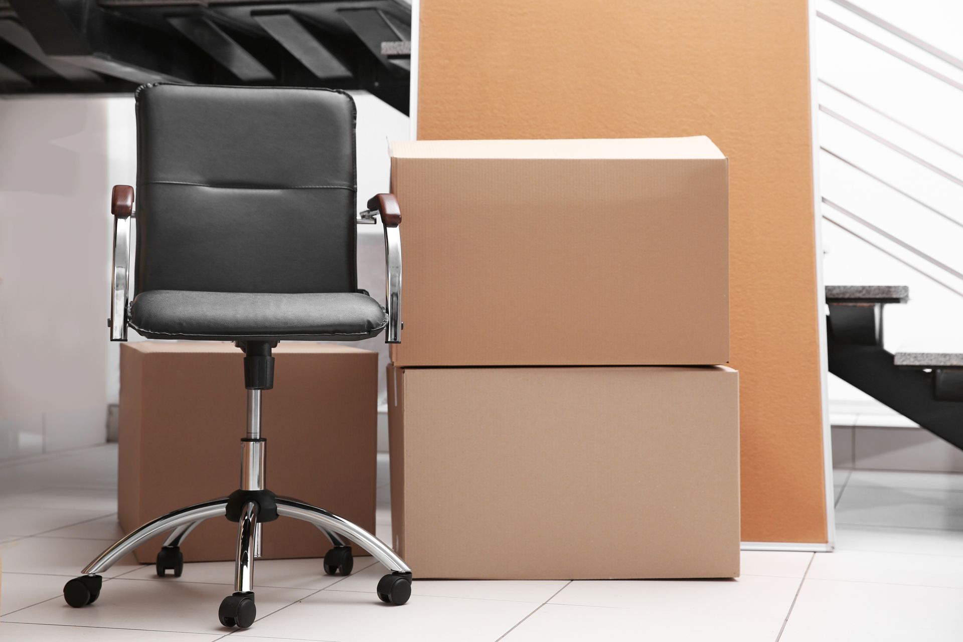 Office chair next to stacked moving boxes, indoors near stairs.
