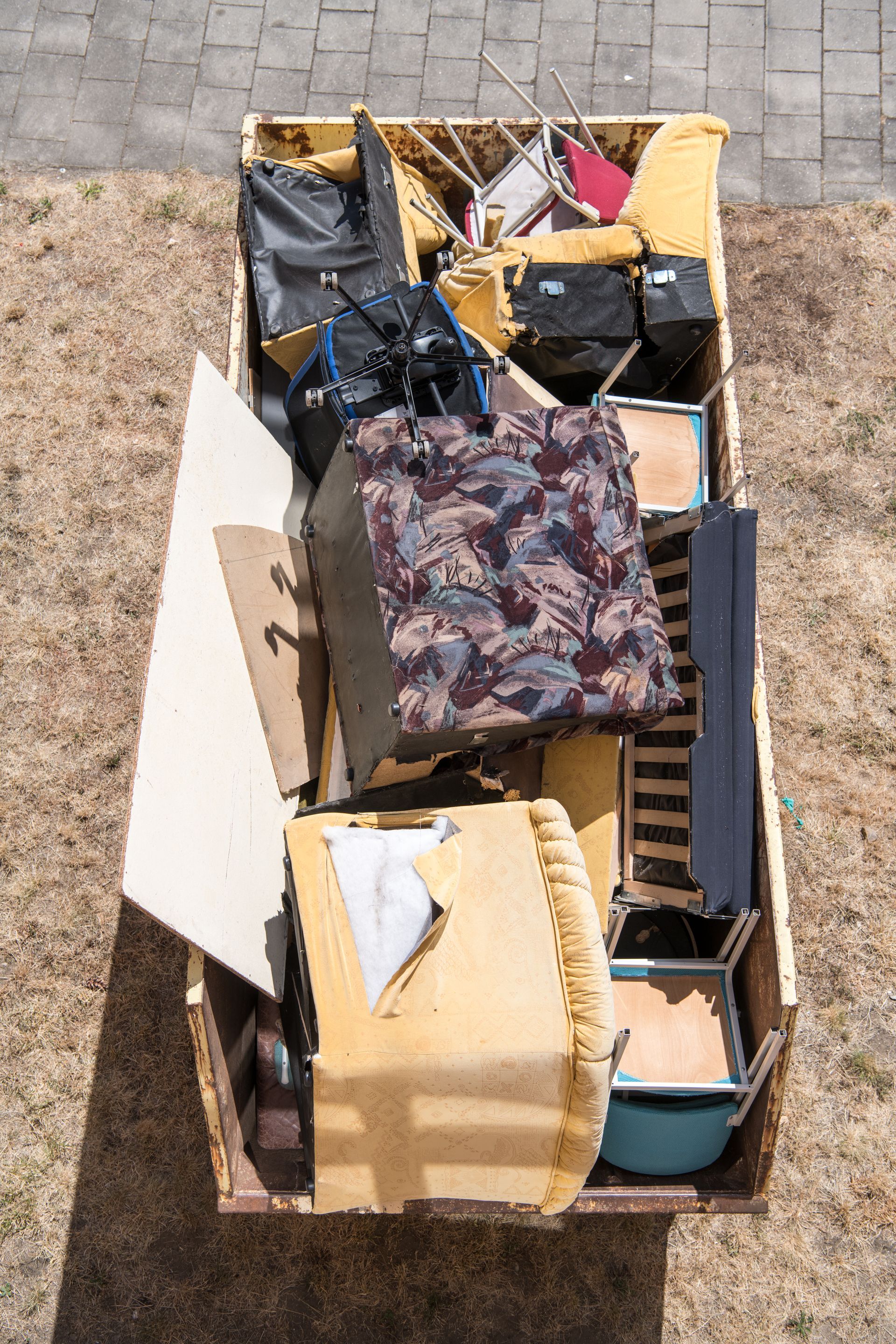 Dumpster overflowing with discarded furniture and objects, outdoors on gravel.