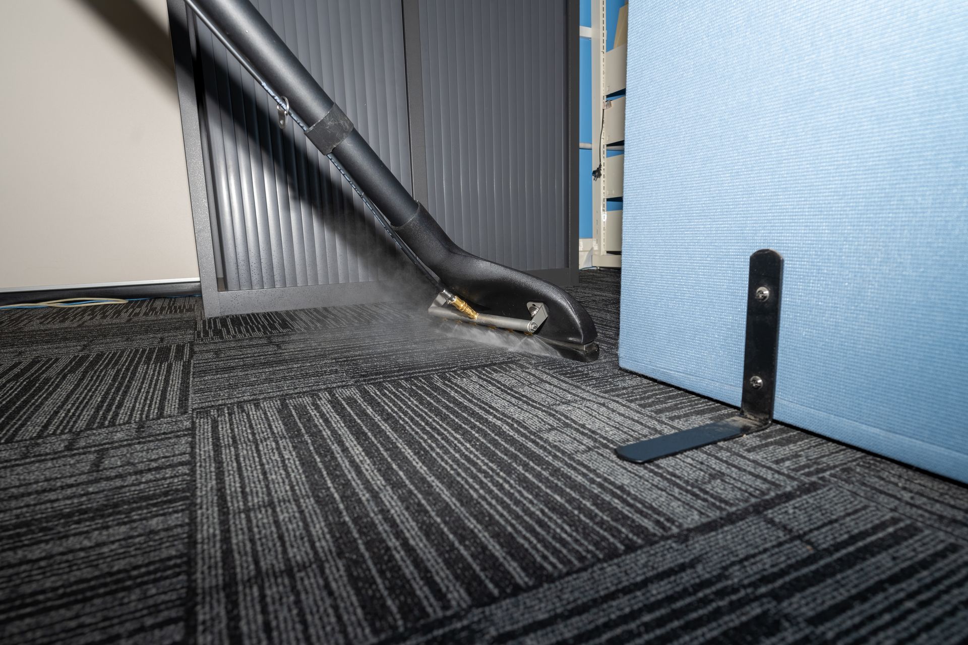 A carpet cleaner cleaning a gray carpeted office floor.
