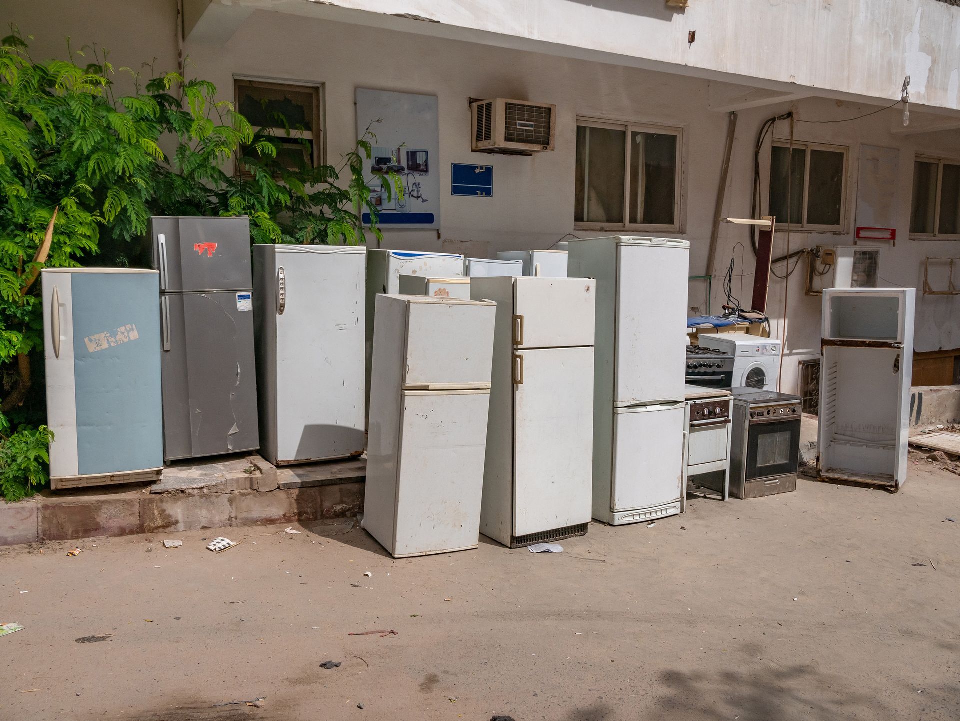 Old refrigerators and appliances lined up outside a building.