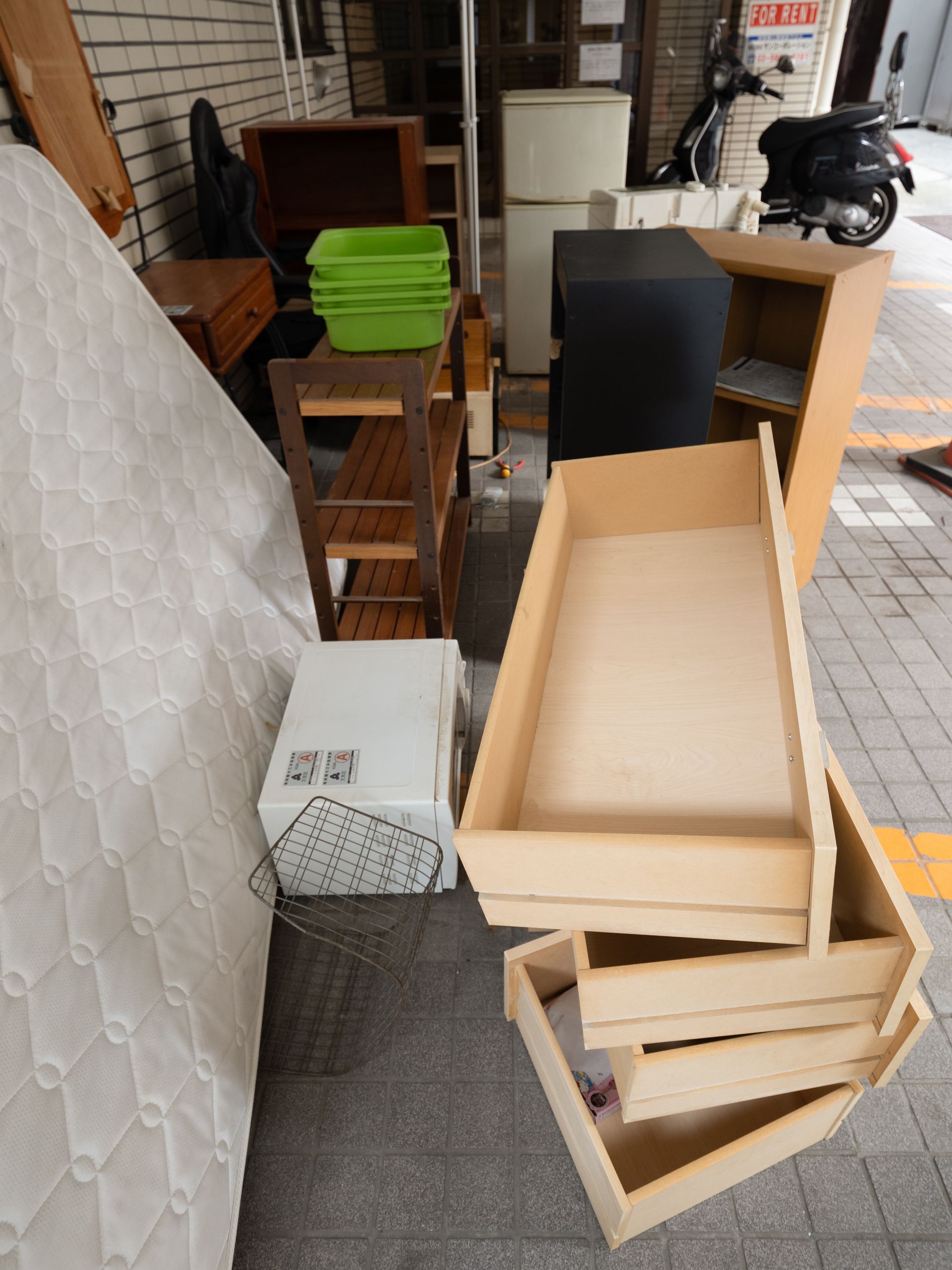 Discarded furniture and appliances on a sidewalk: mattress, drawers, refrigerator, chair, and cabinets.