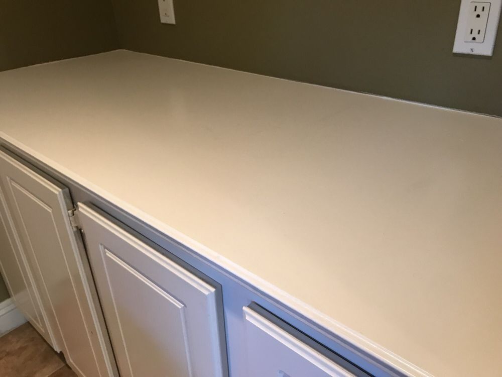 White countertop on white cabinets against a green wall, with electrical outlets.