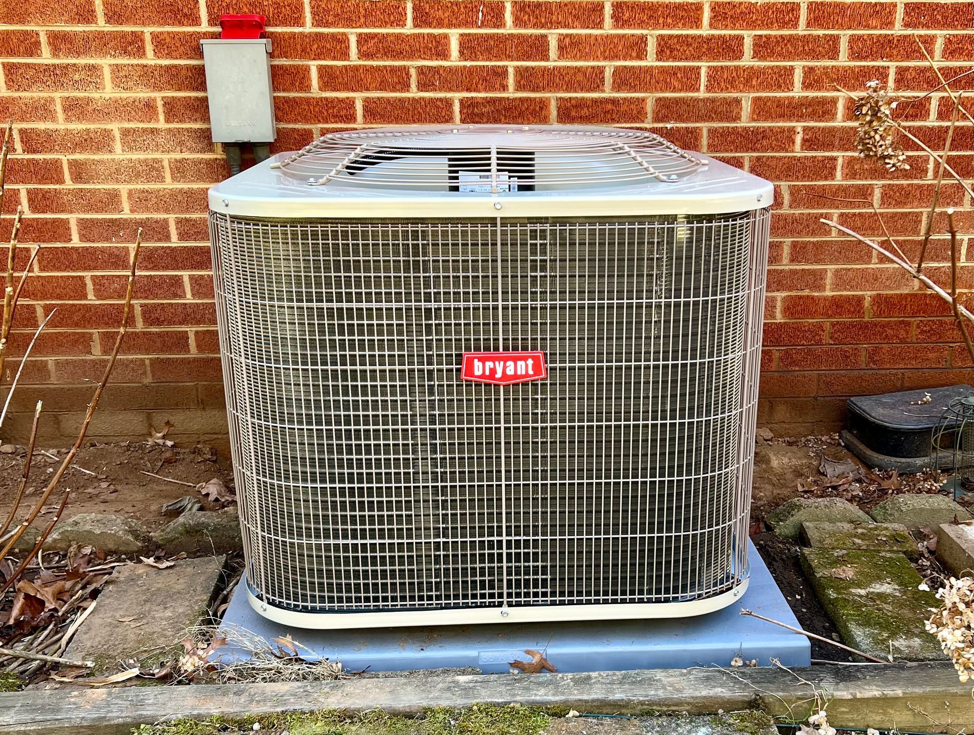 A large air conditioner is sitting in front of a brick wall.