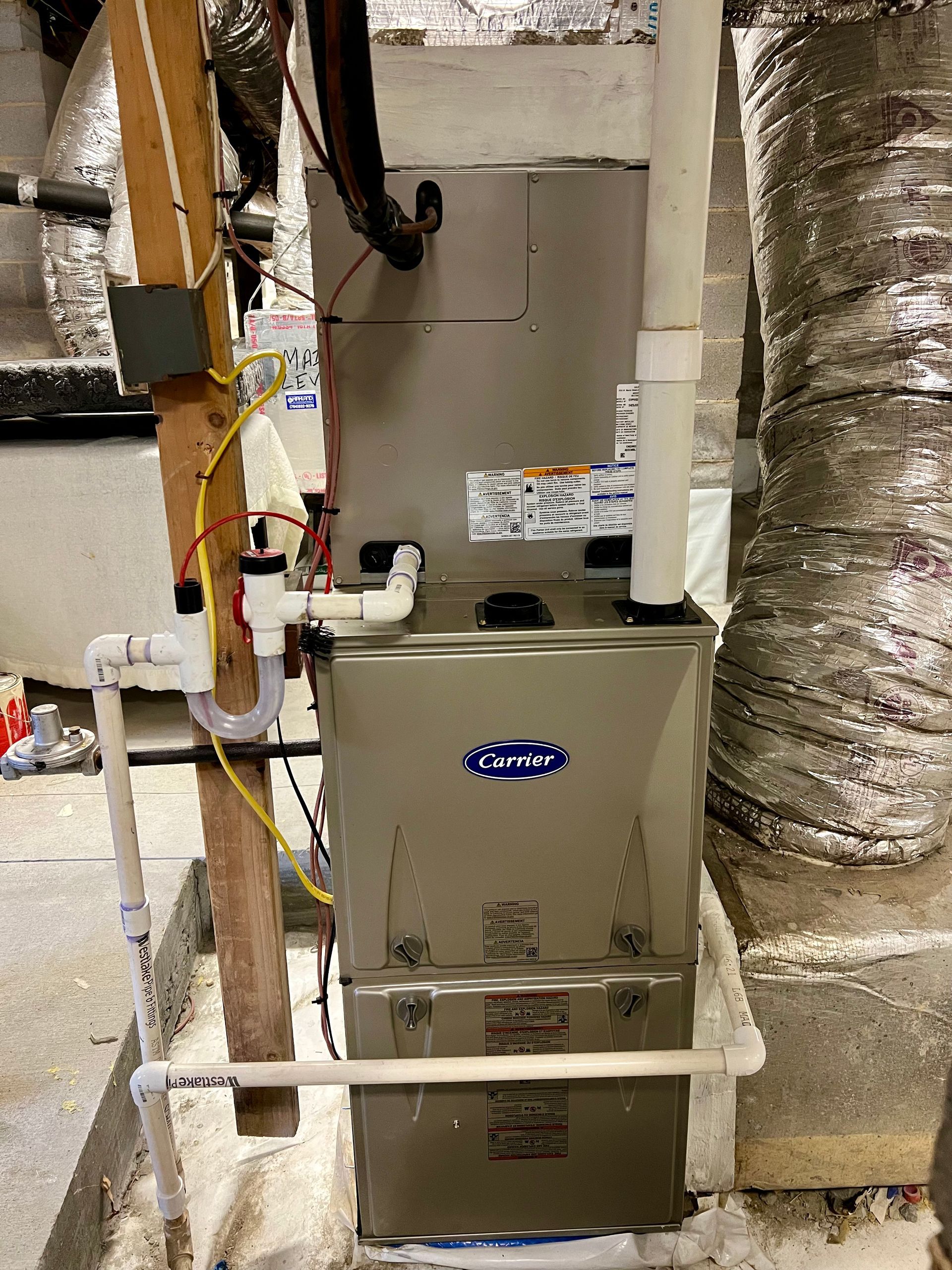 A stainless steel furnace is sitting in a basement next to pipes.