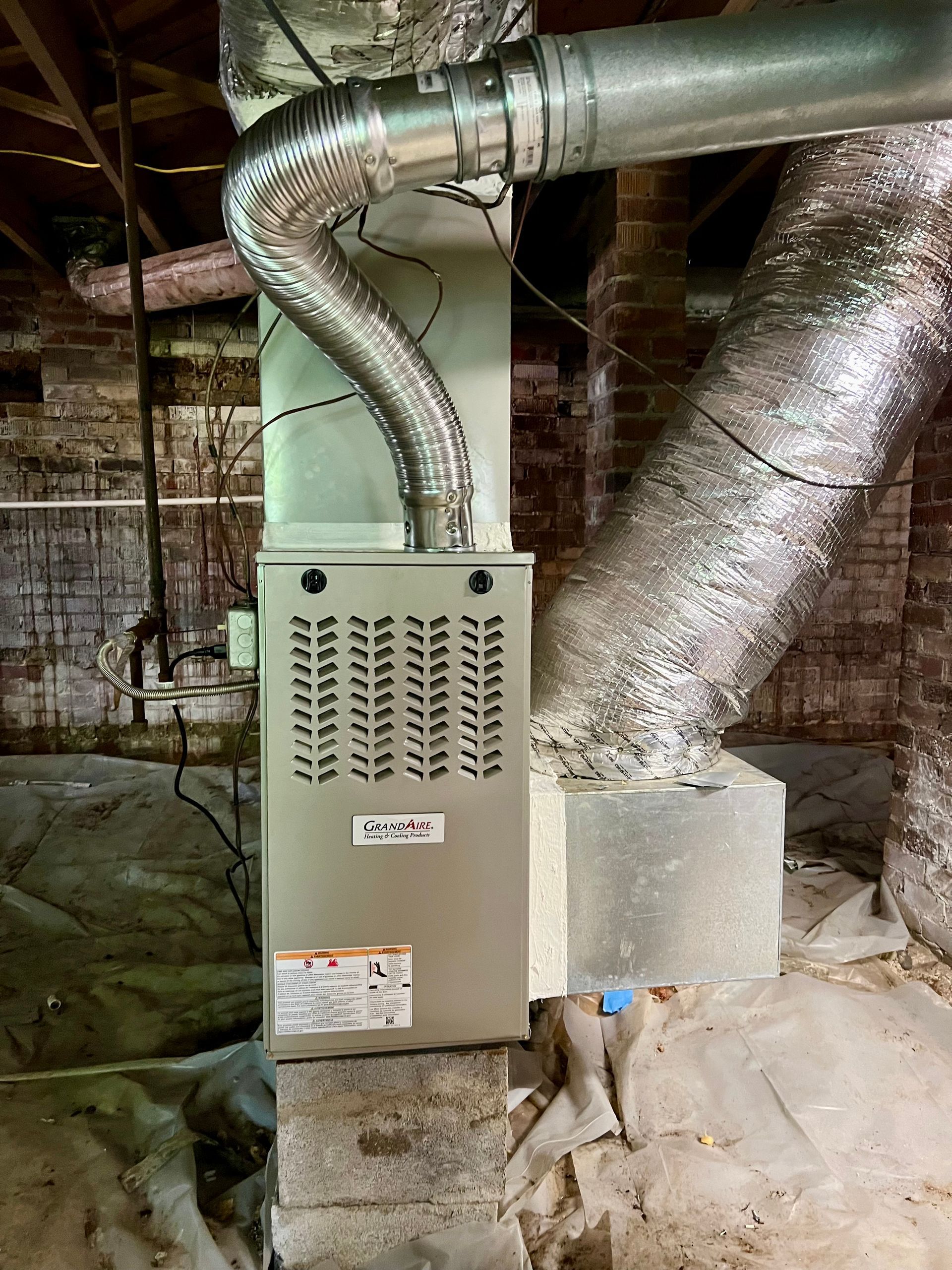 An air conditioner is sitting in a basement next to a brick wall.