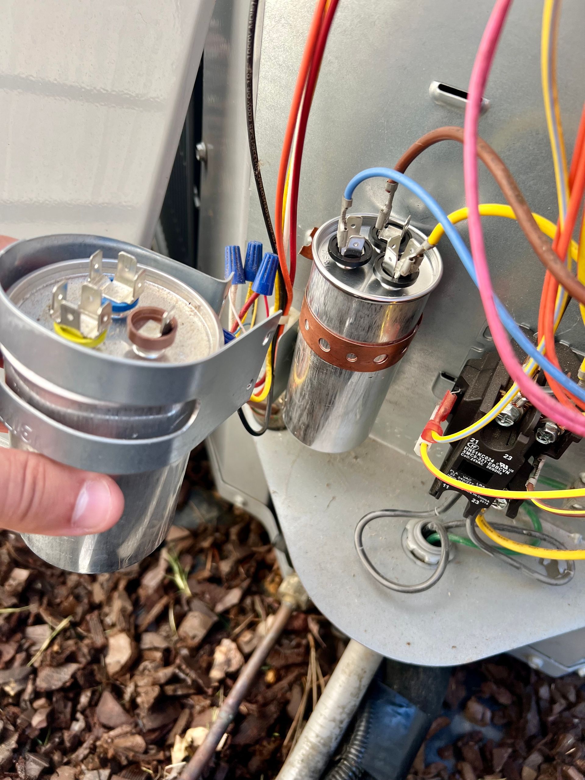 A person is holding a capacitor in front of a bunch of wires