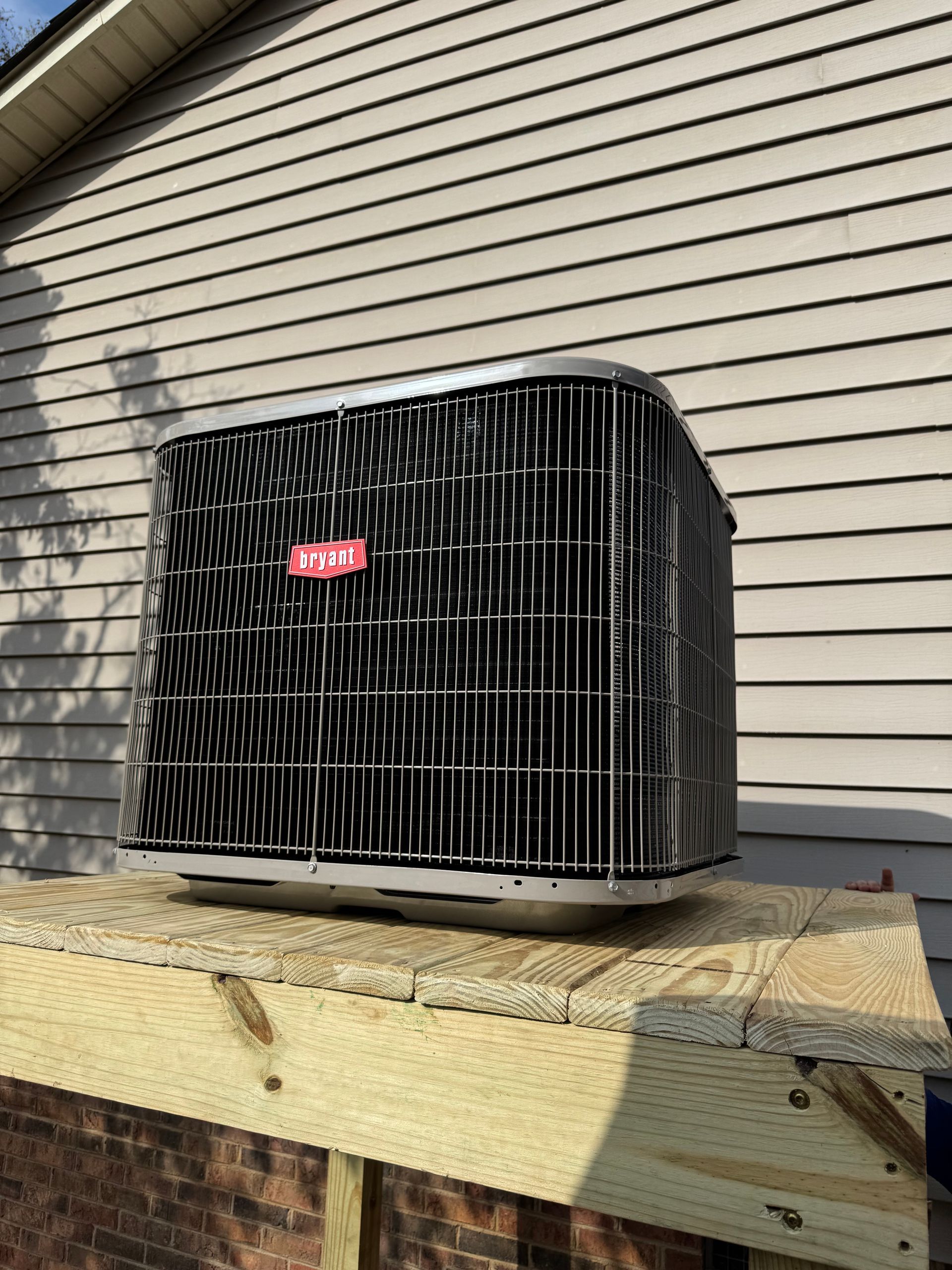 An air conditioner is sitting on top of a wooden shelf in front of a house.