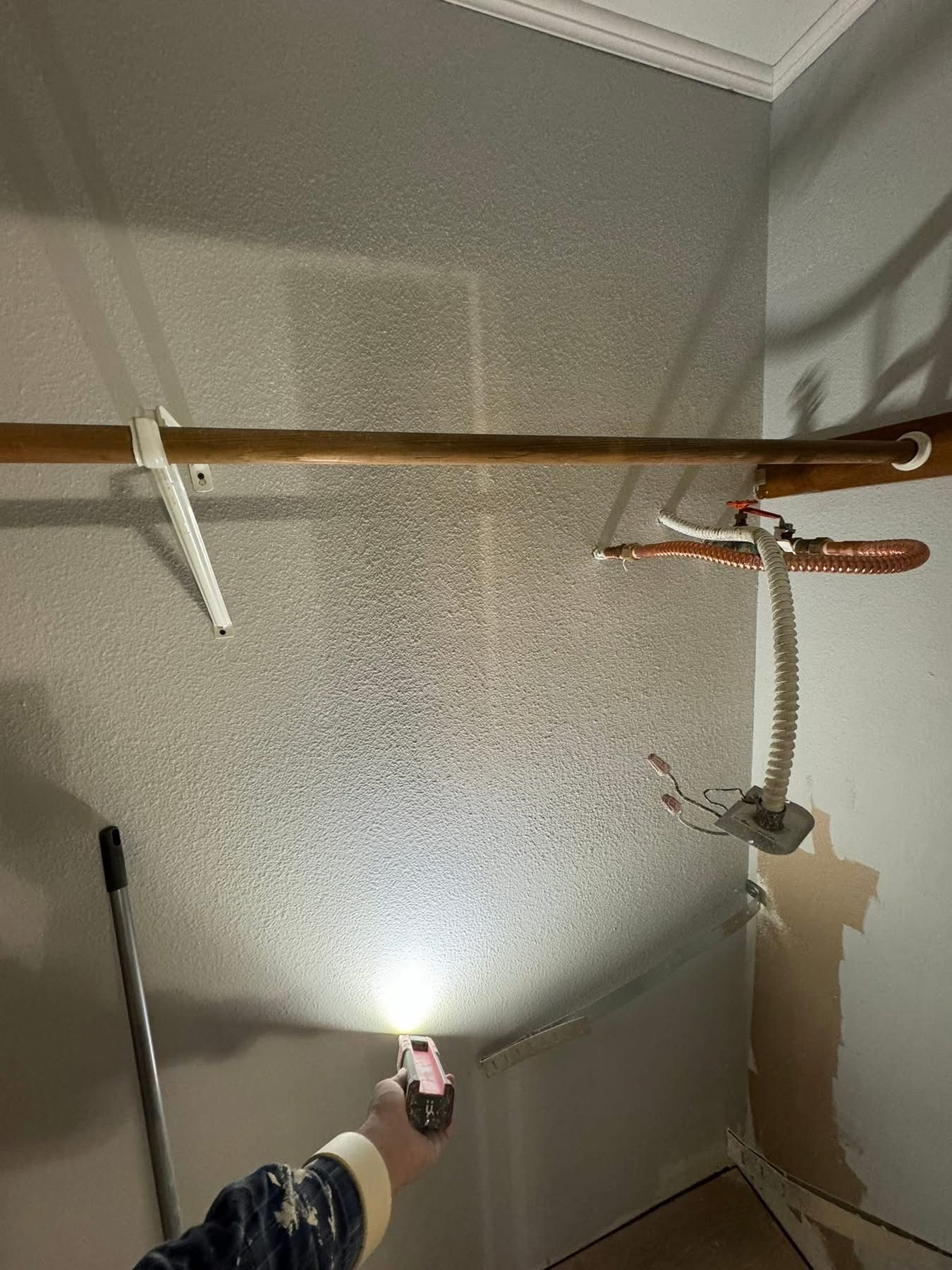 A person shines a flashlight in a corner closet. The walls are speckled. A rod with hangers is mounted.