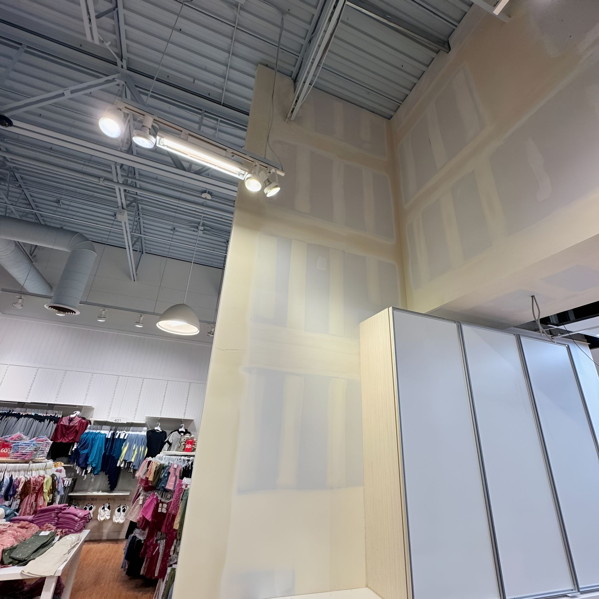 Interior retail space under construction, unfinished walls and exposed ceiling, merchandise visible.