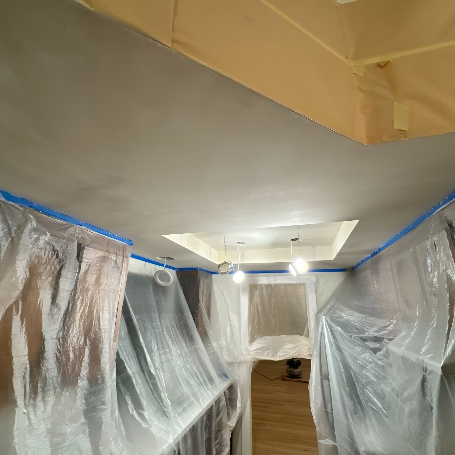 Room covered in plastic and blue tape, likely in preparation for painting or renovation.